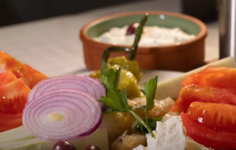 Meze plate of tomato, red onion, pepper, white cheese and olives with a bowl of tarator